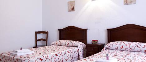 A hotel room with two beds, each with a red and white patterned bedspread, a wooden headboard, and a nightstand with a lamp.