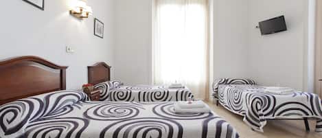 A hotel room with two beds, a TV mounted on the wall, and a window with curtains.