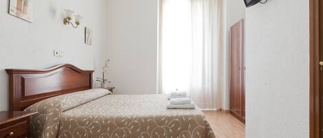 Une chambre d’hôtel avec un lit en bois, une table de chevet, un téléviseur à écran plat fixé au mur et une fenêtre avec des rideaux.