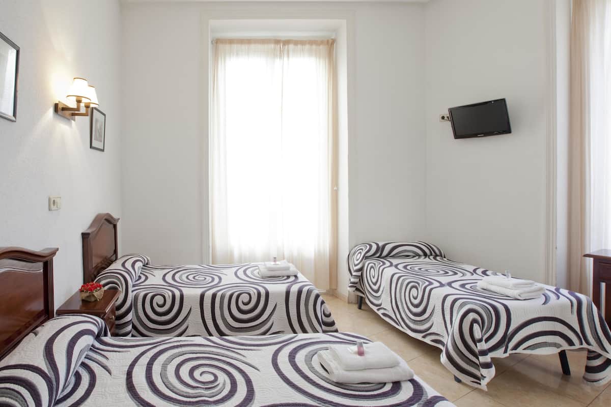 A hotel room with two single beds, a desk, a chair, a TV, and a window with curtains.