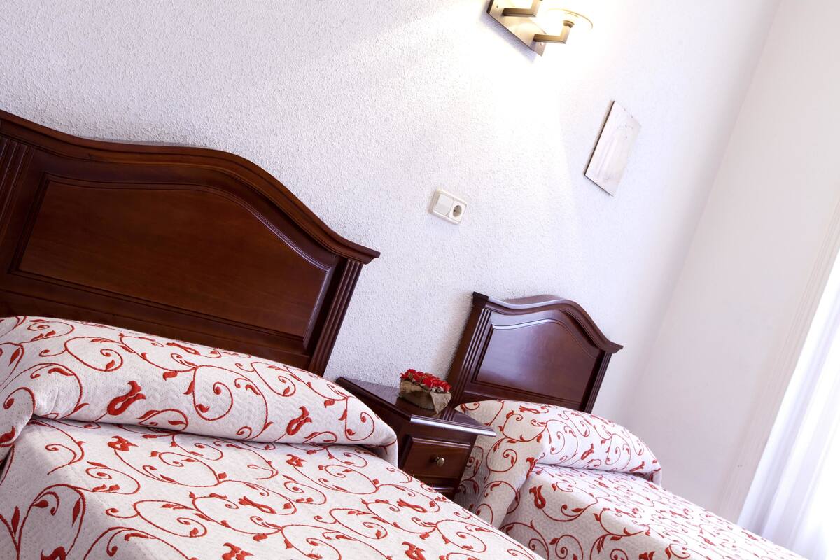 A neatly made bed with patterned bedding, a wooden headboard, and a bedside table with a vase of flowers.