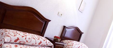 A neatly made bed with patterned bedding, a wooden headboard, and a bedside table with a vase of flowers.