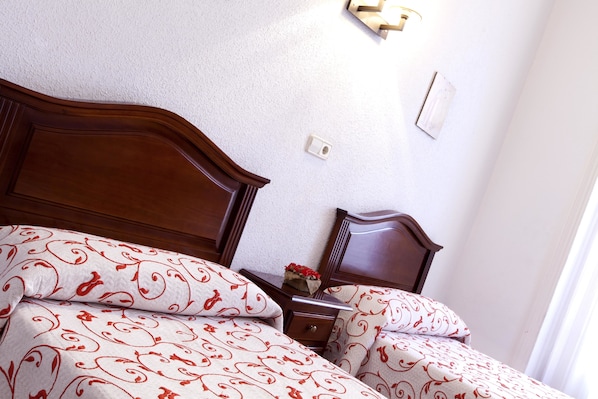 Una cama bien hecha con ropa de cama estampada, un cabecero de madera y una mesita de noche con un jarrón de flores.