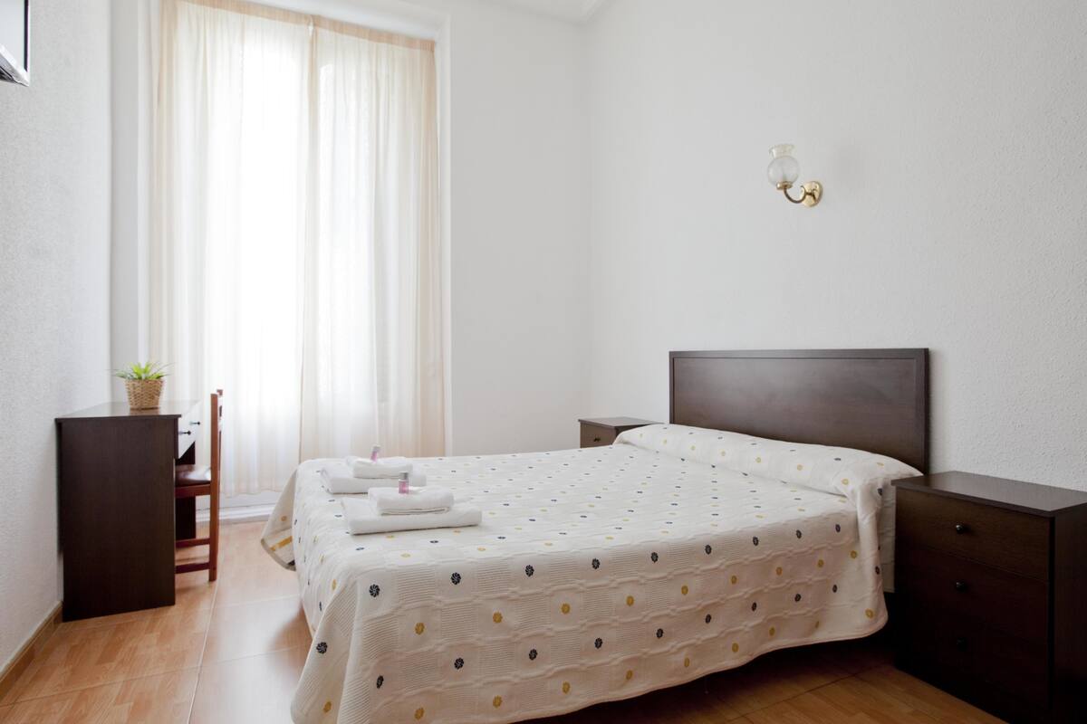 A neatly arranged bedroom with a bed, bedside tables, a chair, and a window with curtains.