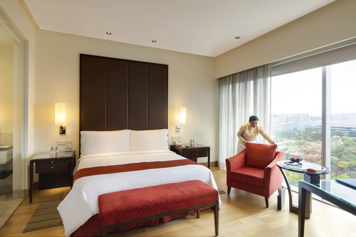 Une chambre d’hôtel avec un grand lit, un fauteuil rouge, une petite table et une vue sur la ville.