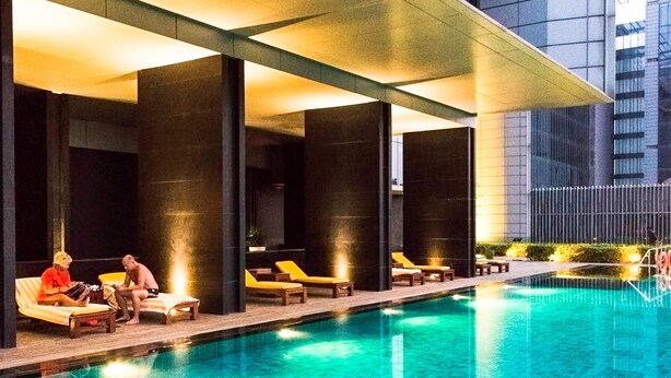 Uma área interna de piscina moderna com piso ladrilhado, cadeiras de lounge e um espaço de estar coberto.