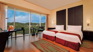 Quarto de hotel com duas camas, uma escrivaninha e uma cadeira, e uma janela grande com vista para o exterior.