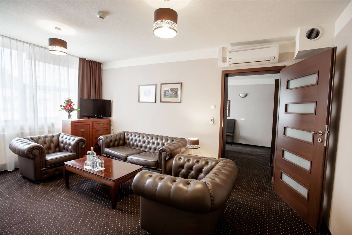 A hotel room with a leather sofa set, a coffee table, a TV, and a door with frosted glass panels.