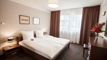 A hotel room with a large bed, a desk, a chair, a lamp, and a vase with flowers.