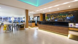 A hotel reception area with a modern design, featuring a reception desk, seating area, and a view of the city through large windows. - Hotéis Le Canard (Lages)