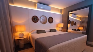 A modern hotel room with a large bed, two bedside tables with lamps, a wall-mounted air conditioner, and decorative wall plates. - Hotéis Le Canard (Lages)