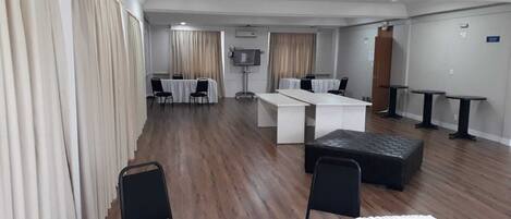 Quarto de hotel com uma cama grande, uma escrivaninha, duas cadeiras, uma mesa pequena e uma televisão.