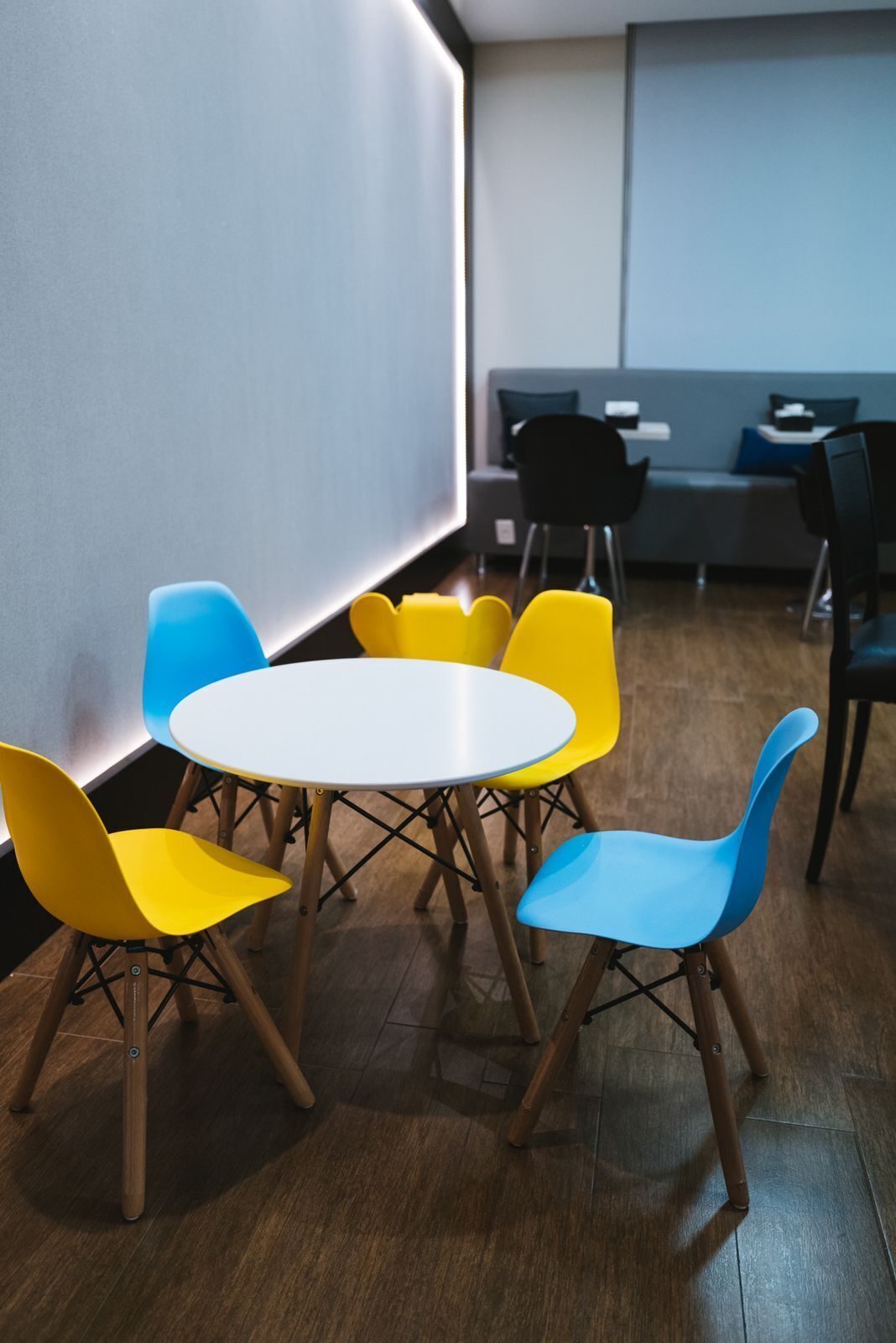 A modern meeting room with a round table and six chairs, wooden floors, and a grey sofa in the background.