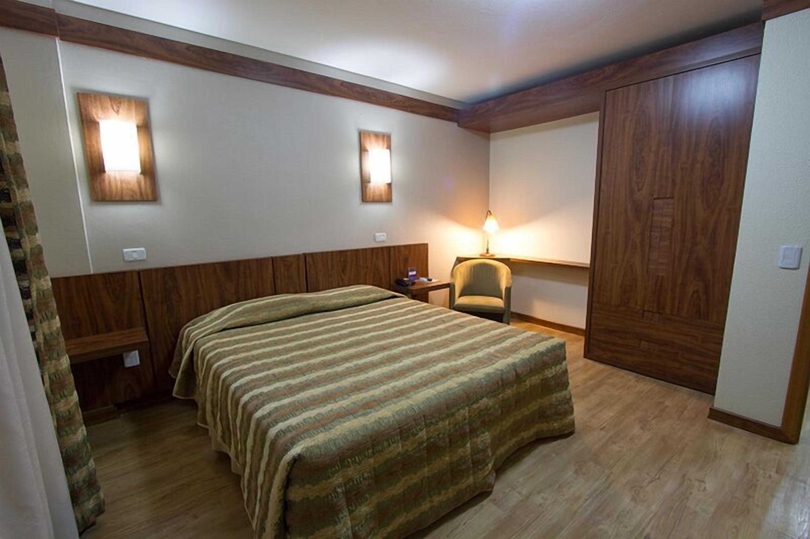 Een slaapkamer met een bed, nachtkastje, stoel en kledingkast.