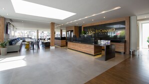 A modern hotel lobby with a reception desk, seating area, and large windows. - Hotéis Le Canard (Lages)