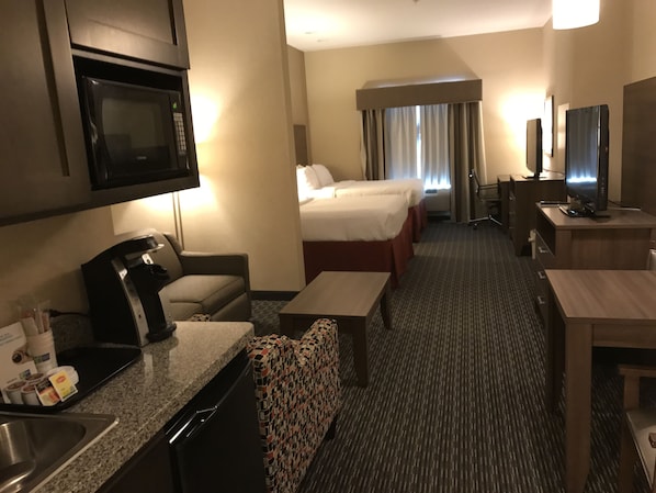 A hotel room with a kitchenette, a bed, a desk, and a TV.