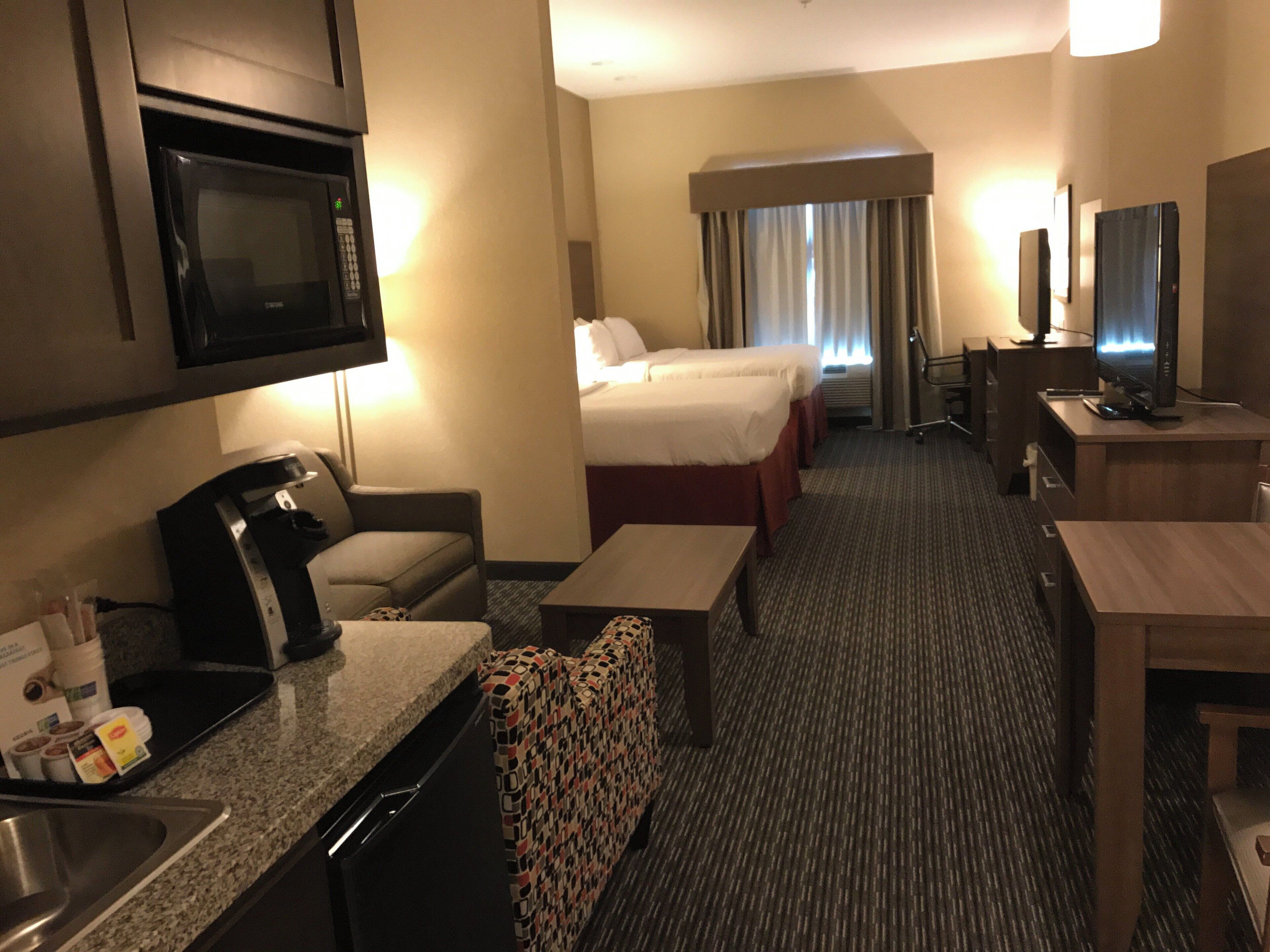 Una habitación de hotel con kitchenette, cama, escritorio, televisor y baño.