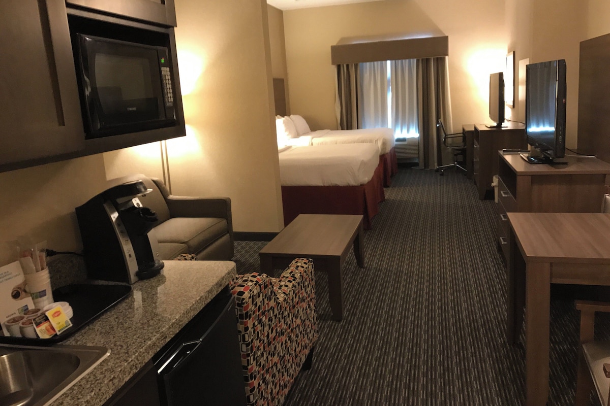 A hotel room with a kitchenette, a bed, a desk, a TV, and a bathroom.