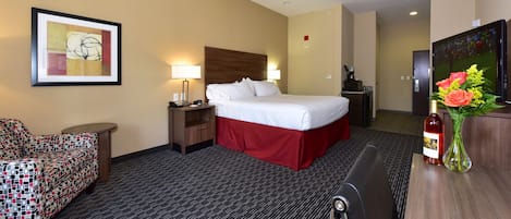 Une chambre d’hôtel avec un lit, un bureau, une chaise, une lampe, un tableau encadré, une télévision et un vase avec des fleurs.