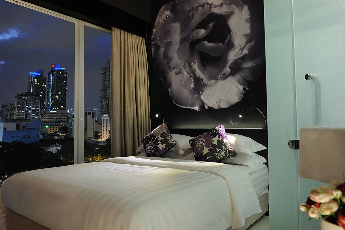 A hotel room with a large bed, a city view, and a unique wall art piece.