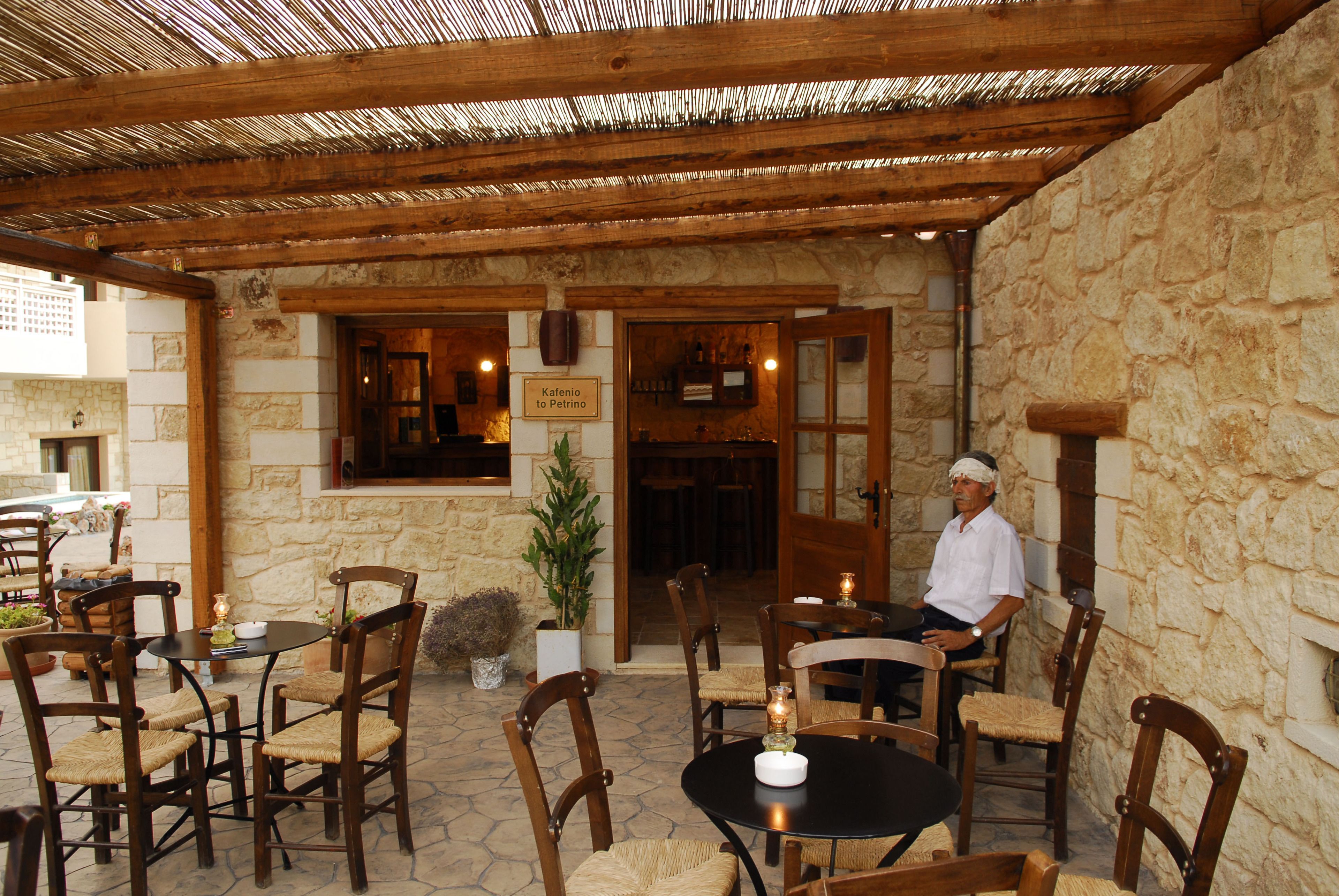 An outdoor patio with stone walls, wooden furniture, and a man sitting at a table.