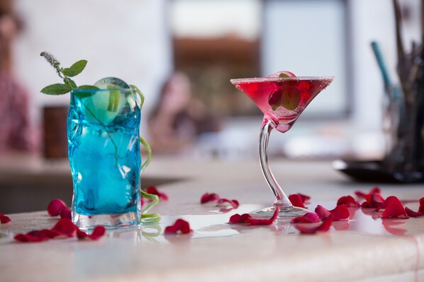 Dos bebidas sobre una mesa, con pétalos de rosa esparcidos alrededor.