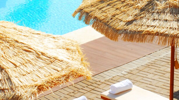 Un área de piscina con sillones de descanso y sombrillas de paja.