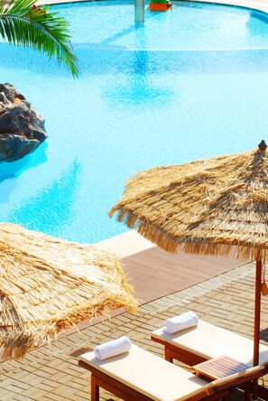 Un área de piscina con sillones de descanso y sombrillas de paja.