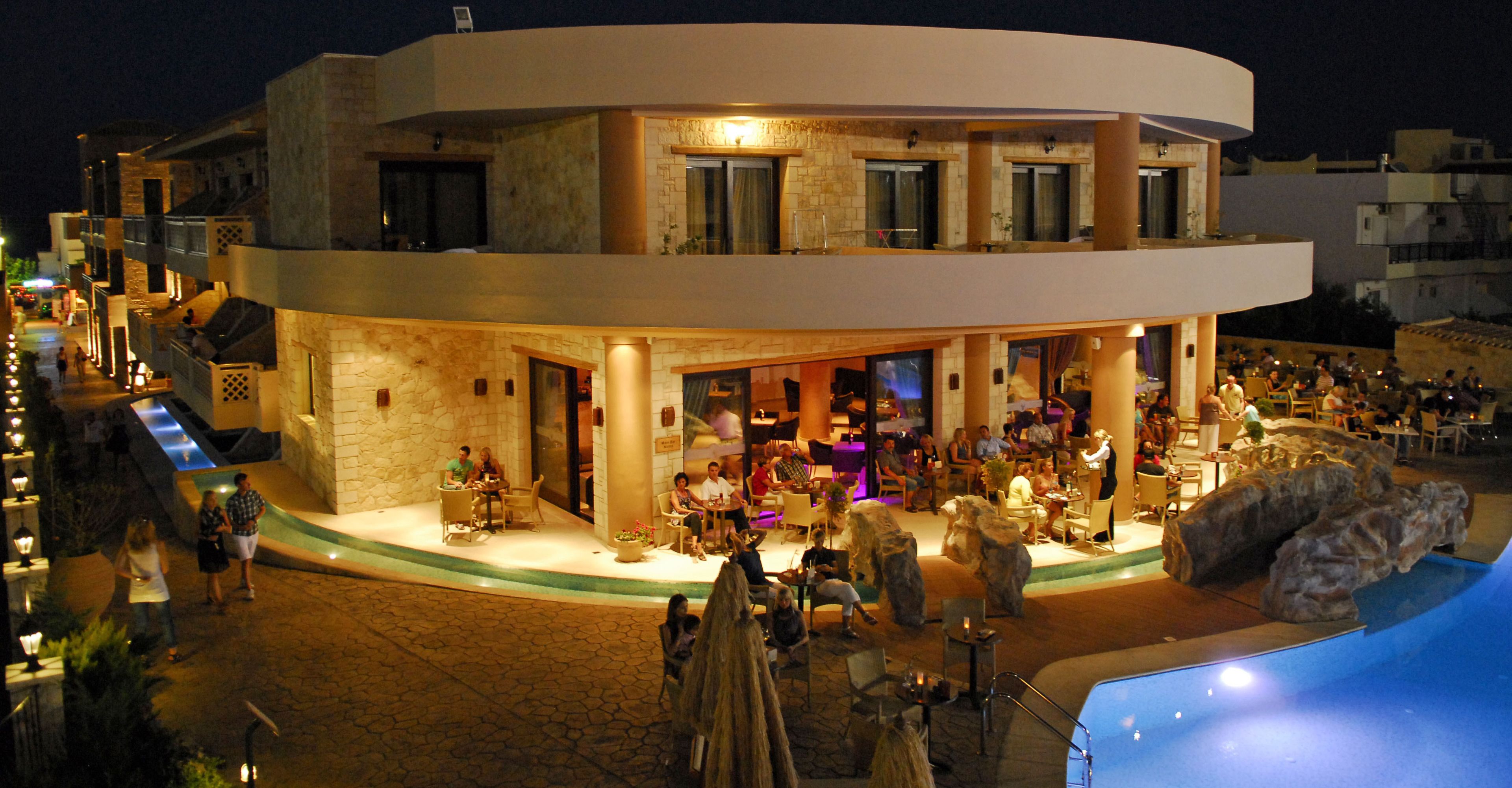 Een hotel met een gebogen gevel, een terras buiten en een zwembad.