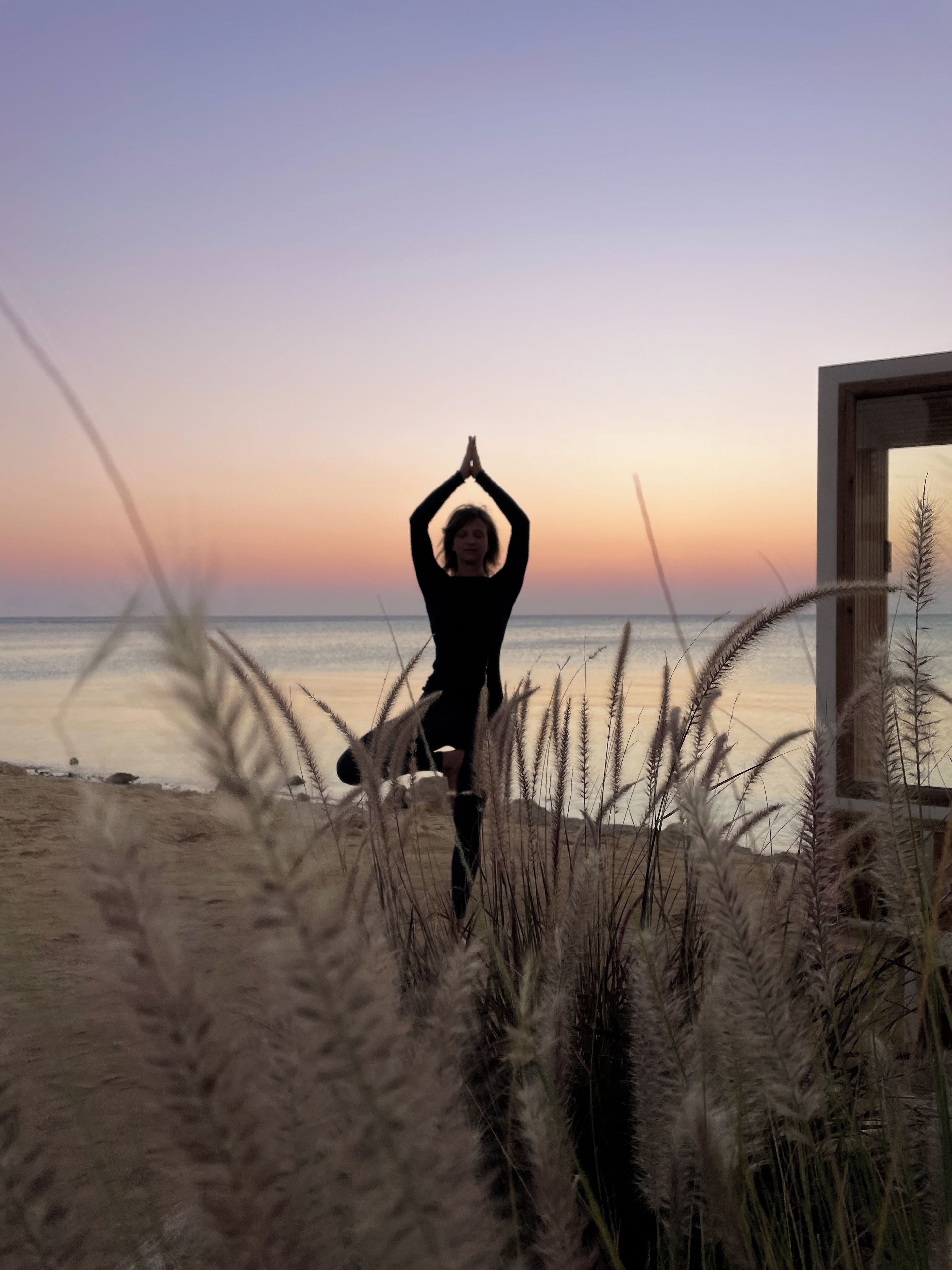 A person performing a yoga pose on a beach with a sunset in the background.
