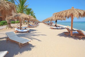 A beach with rows of sun loungers and thatched umbrellas, palm trees, and a clear blue sky. - The Breakers Diving & Surfing Lodge (Soma Bay)