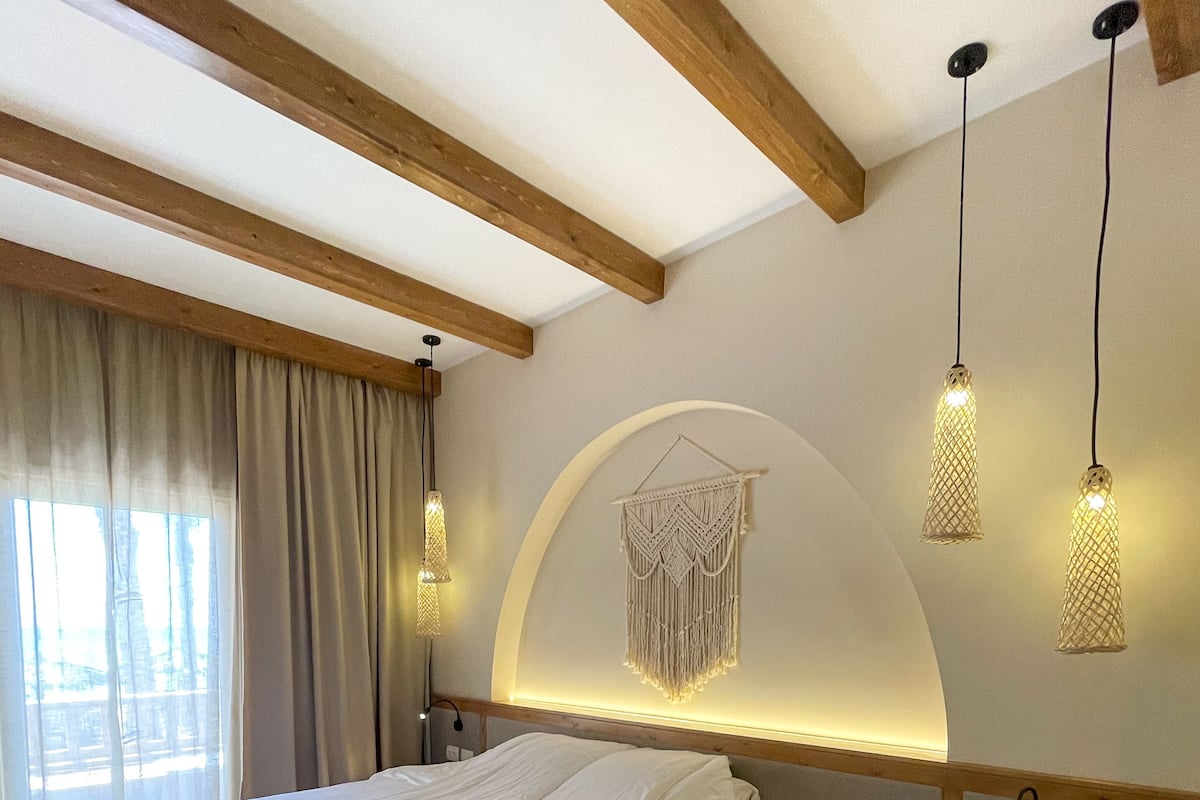 A modern hotel room with a large bed, wooden beams, a bedside phone, and a decorative wall hanging.