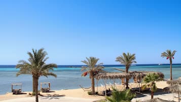 A beach with palm trees, a thatched-roof structure, and a clear blue sea.
