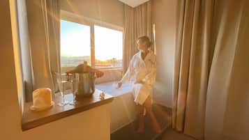 Una persona en un albornoz blanco sentada junto a una ventana con vista al atardecer.