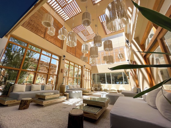 A spacious living area with large windows, wooden ceiling beams, and hanging light fixtures.