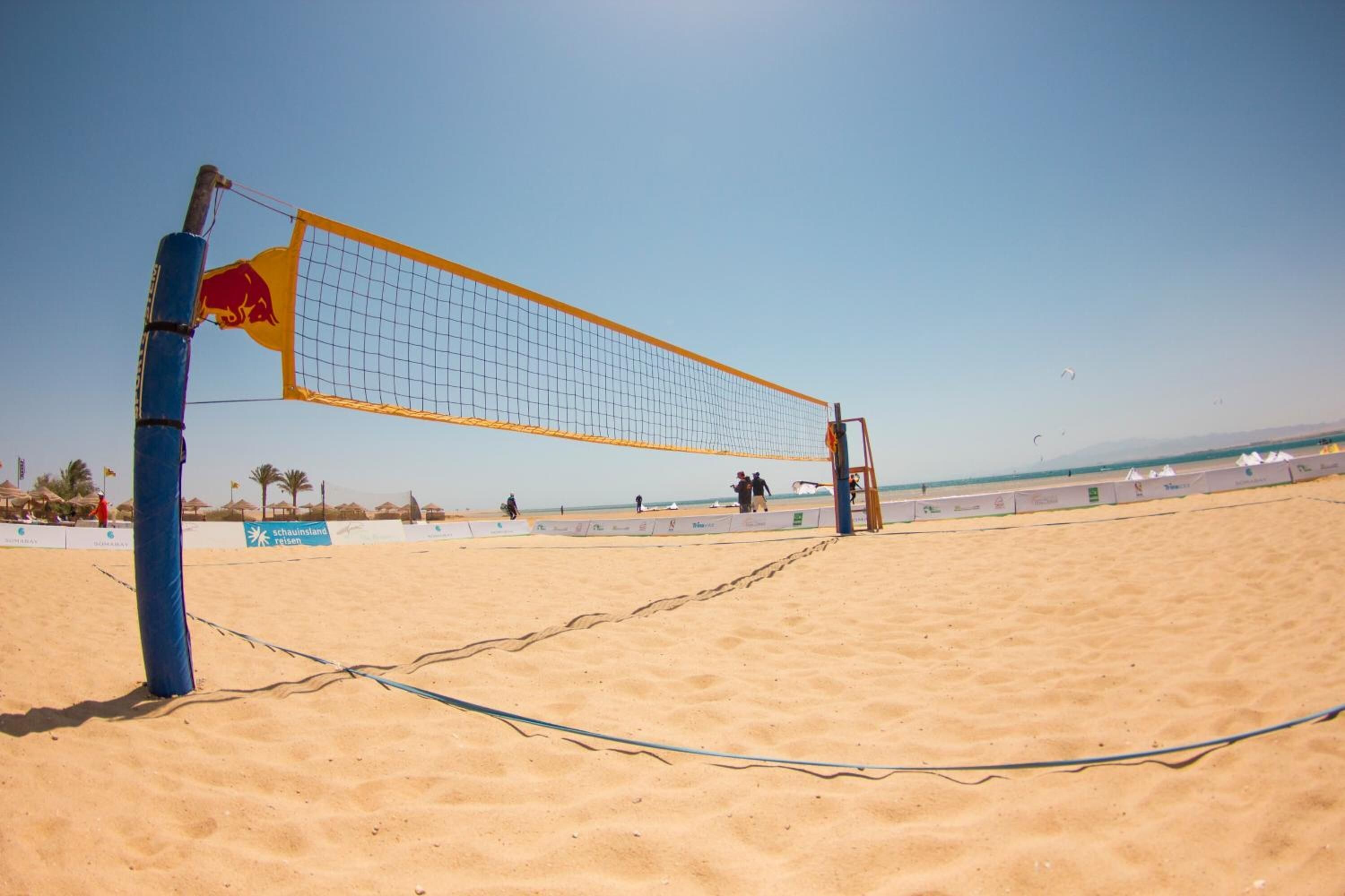 A beach volleyball net with a Red Bull logo, set up on a sandy beach with a clear sky.