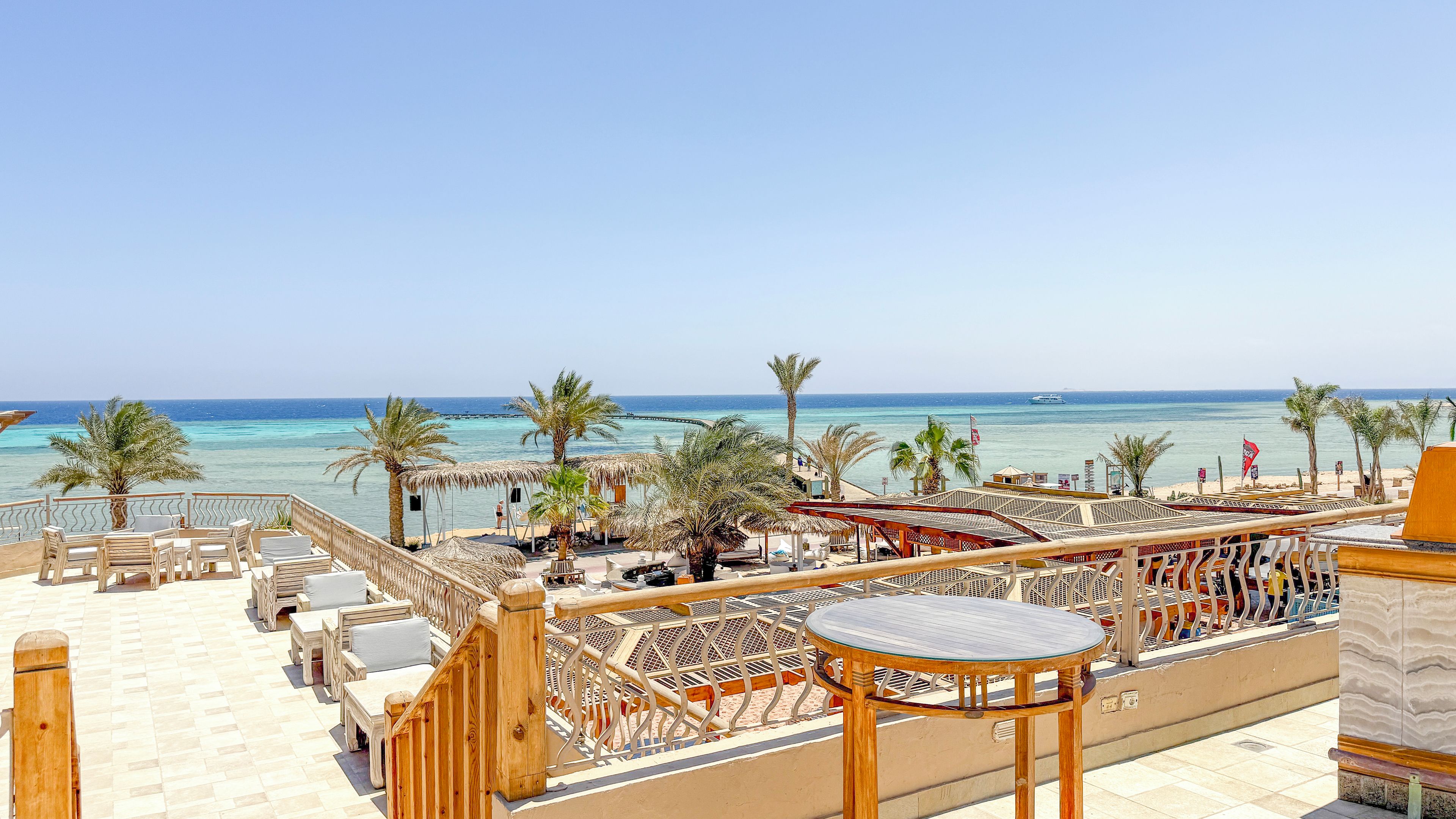 A terrace with outdoor seating, palm trees, and a view of the sea.