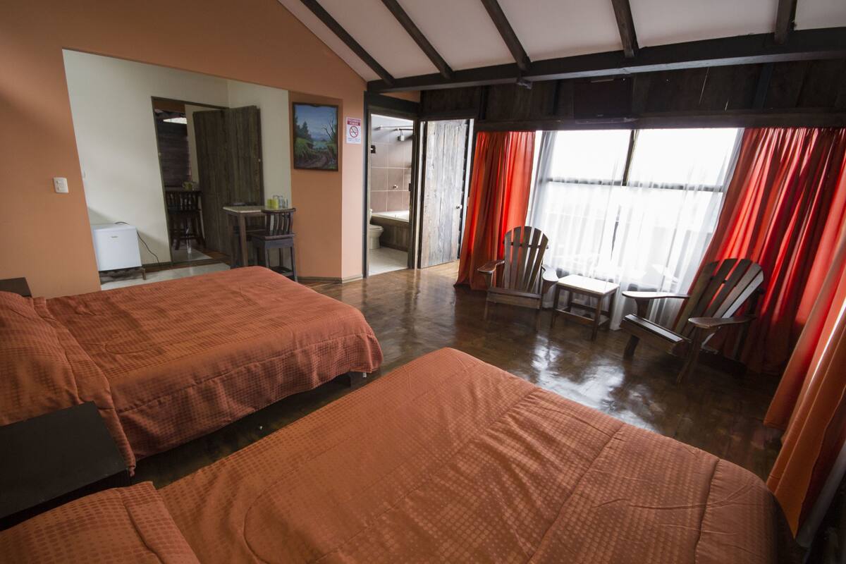 A room with two beds, a desk, and a chair. There is a bathroom visible through an open door.