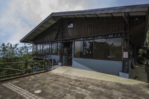 A building with a metal roof and large windows, a staircase leading up, and a paved entrance area. - Hotel Alto Palomo (Toro Amarillo)