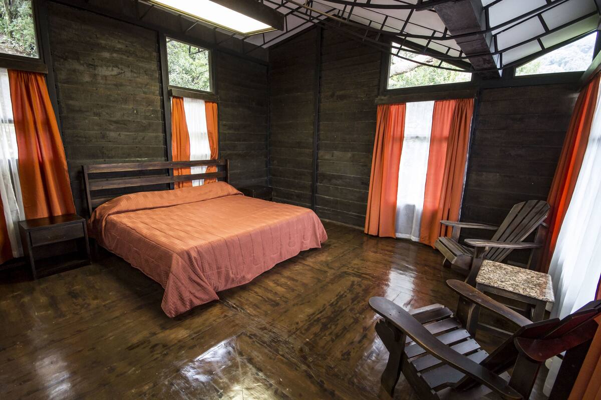 A wooden room with a bed, a chair, and a table.