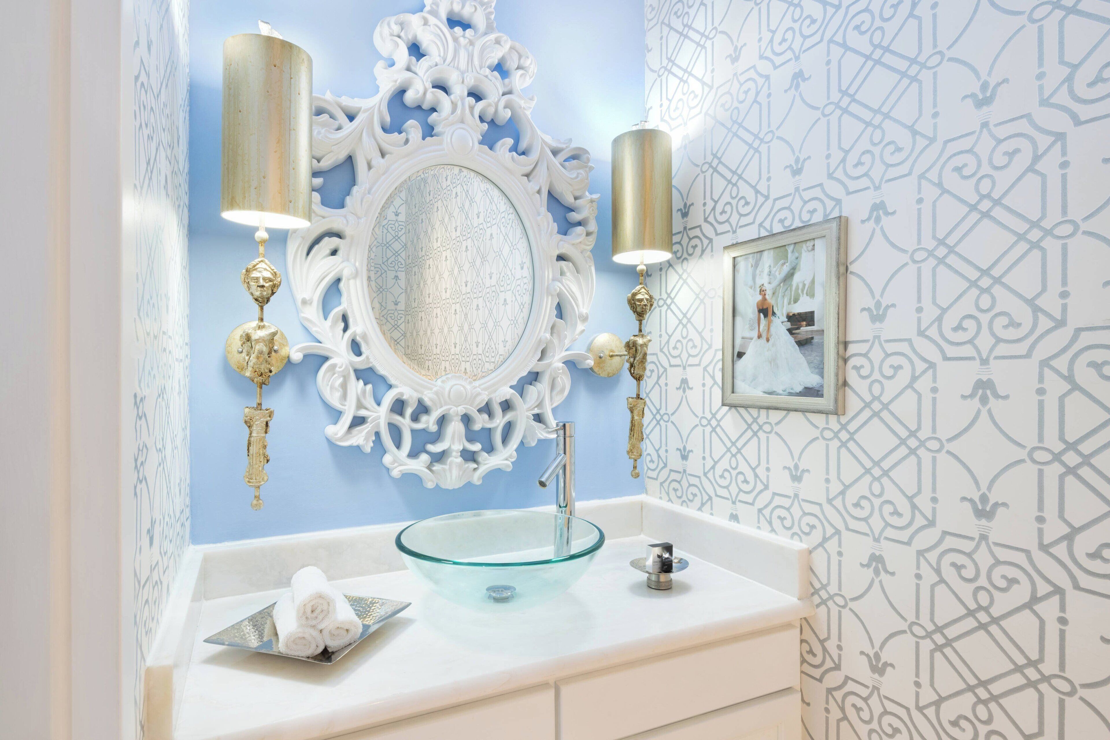 A bathroom with a glass bowl sink, ornate mirror, and wall sconces.