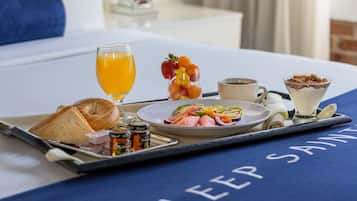 A breakfast tray with toast, fruit, a glass of orange juice, a cup of coffee, and a dessert on a bed with a blue blanket labeled "SLEEP SAI".