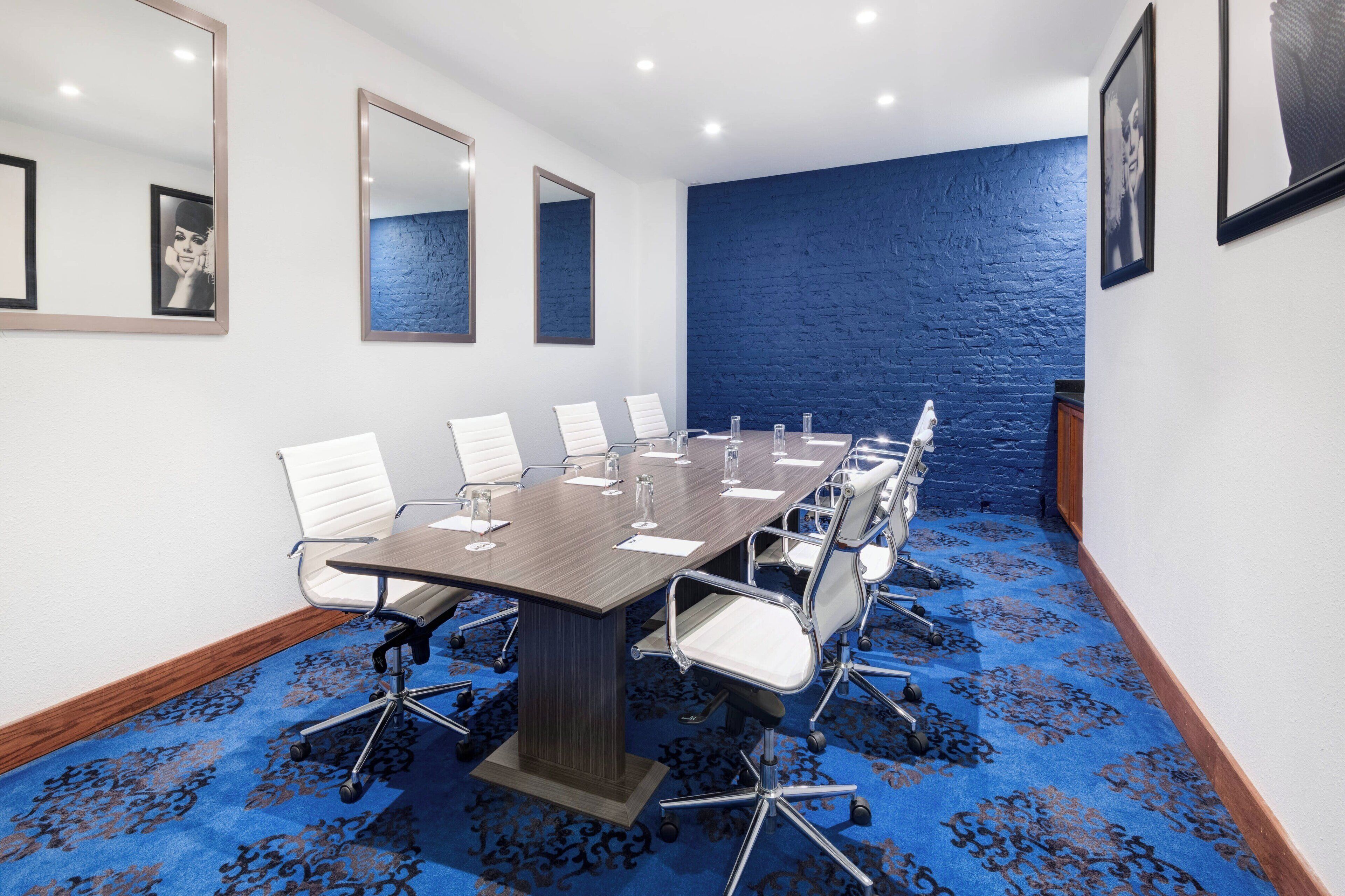 Ein Konferenzraum mit einem langen Tisch, weißen Stühlen und einem blauen Teppich.