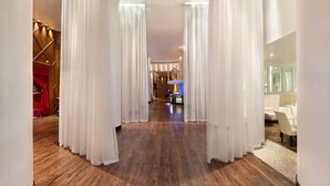 A hallway with wooden flooring, white curtains, and a blue table in the distance. - The Saint Hotel, New Orleans, French Quarter (New Orleans)