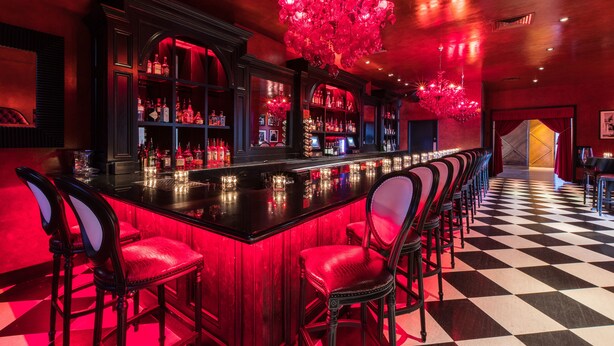 A bar area with a long counter, multiple bar stools, and a chandelier. - The Saint Hotel, New Orleans, French Quarter (New Orleans)