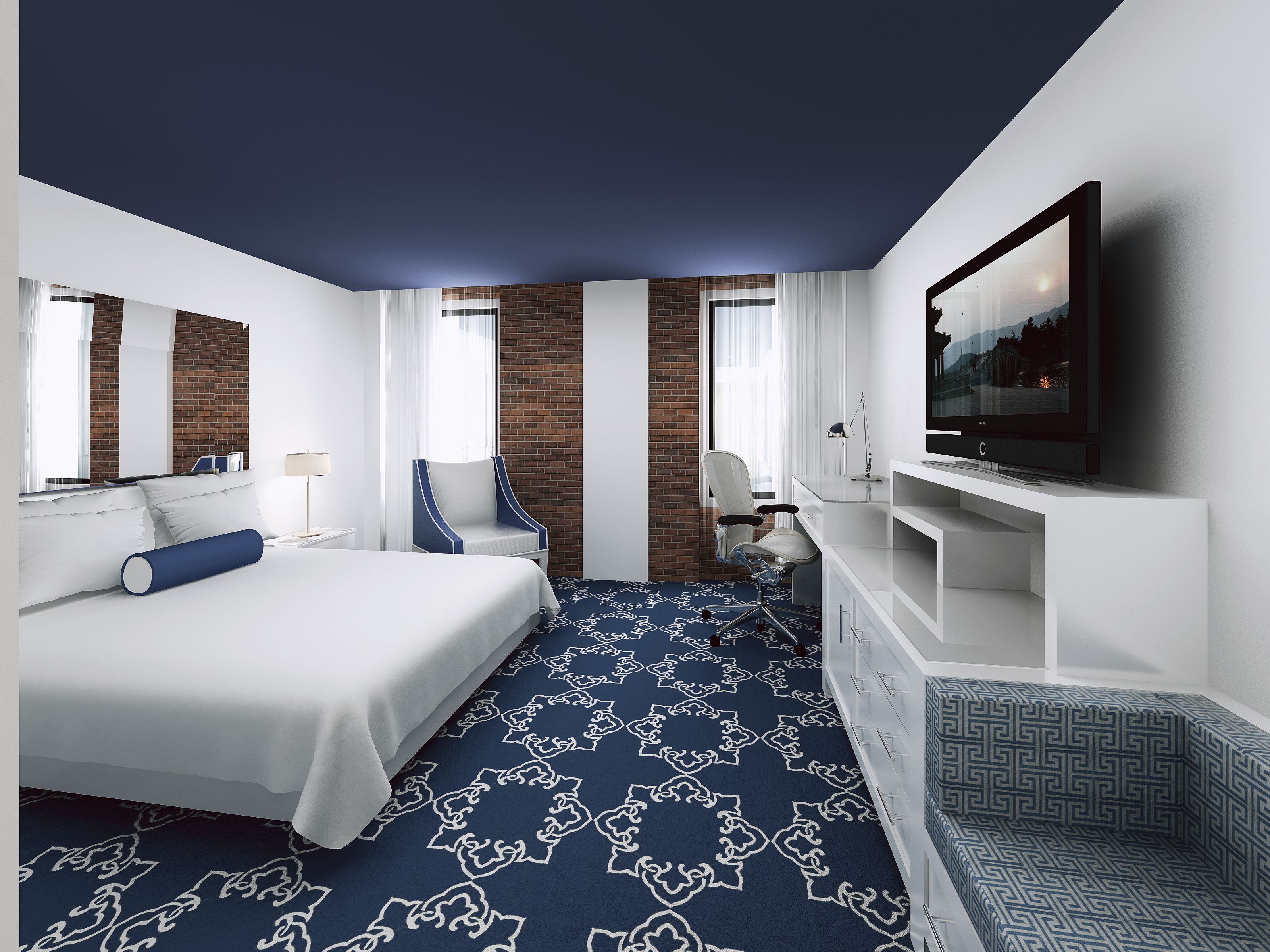 A modern hotel room with a large bed, a desk, a chair, a TV, and a patterned carpet.