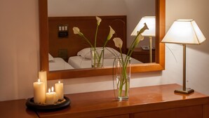 Una habitación de hotel con un escritorio de madera, un espejo, velas y un florero con flores.