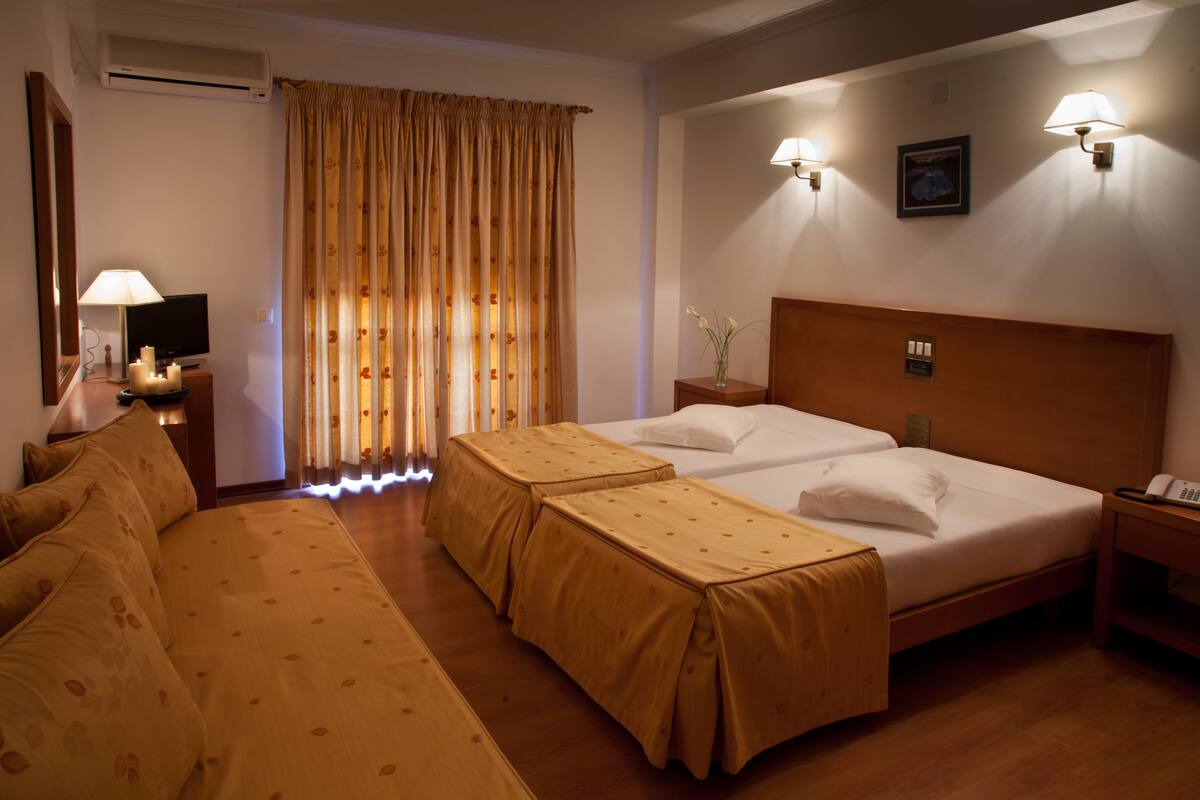 A hotel room with two beds, a sofa, a TV, and a lamp.