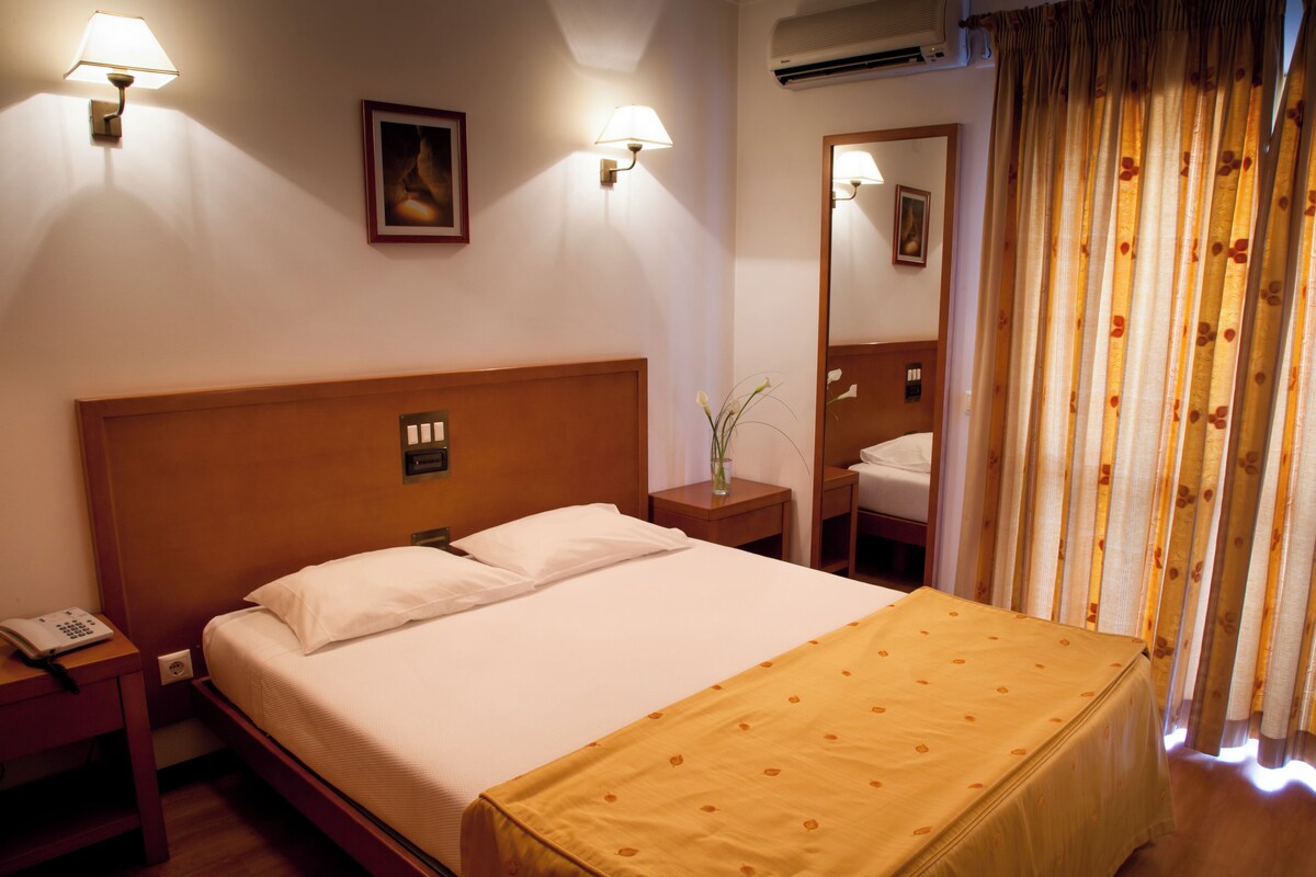 Una habitación de hotel con cama, mesitas de noche, un espejo y una ventana con cortinas.