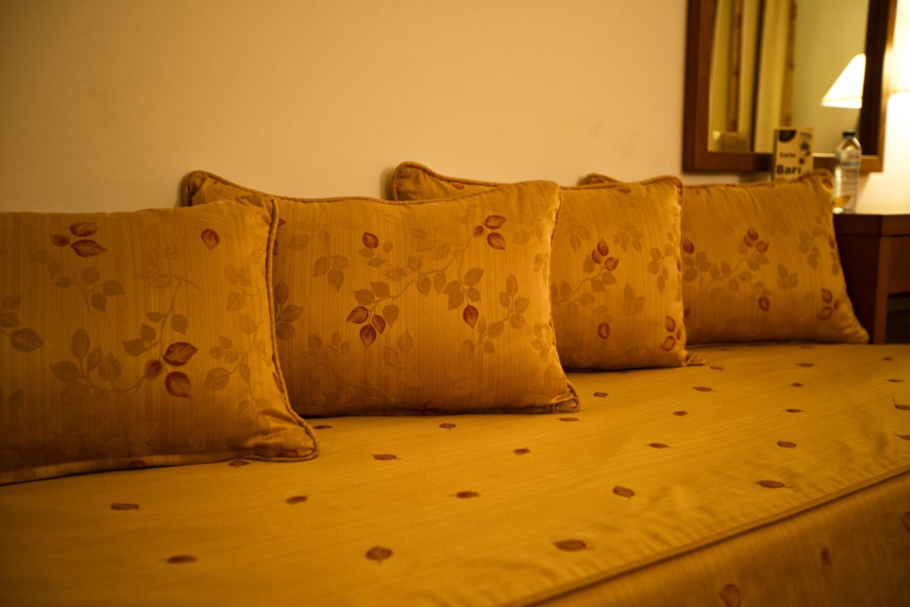 A bed with a yellow floral bedspread and matching pillows.